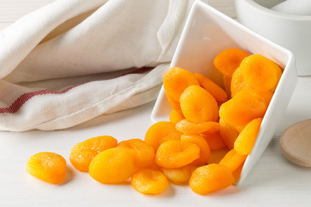 Whole dried apricots fruit in white bowl on white wooden table backgroundの写真素材