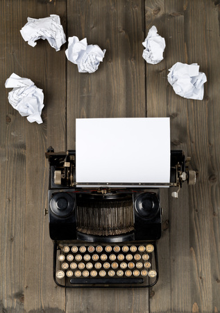Vintage typewriter top down flatlay shot from above with empty, blank sheet of paper and crumbled paper balls on wood table backgroundの写真素材