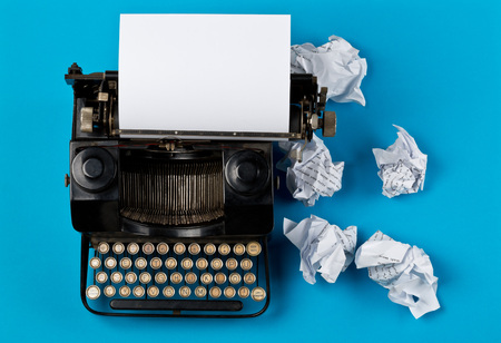 Vintage typewriter top down flatlay shot from above with empty, blank sheet of paper and crumbled paper balls on cyan backgroundの写真素材
