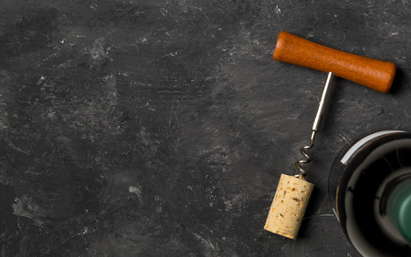 Corkscrew with wine cork and bottle of wine on dark wooden board background, flat lay top view with...