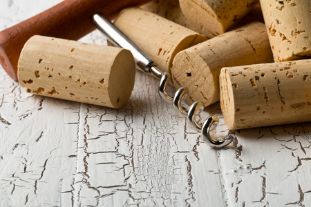 Heap of unused, new, brown natural wine corks with corkscrew on white wooden board background