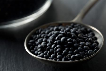 Heap of black organic beluga lentils in metal spoon on black stone background with selective focusの写真素材