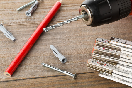 Wall plug dowel with screw, electric power drill, folding rule and pencil on wooden table - home...