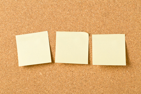 Three empty yellow sticky paper memo notes on cork board with copy space