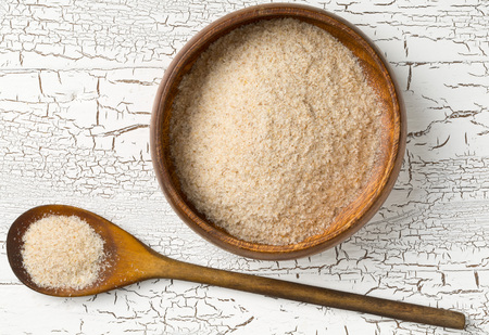 Heap of psyllium husk also called isabgol in wooden bowl and spoon on white table background. Psyllium husk also called isabgol is fiber derived from the seeds of Plantago ovata plant found in India. Flat lay from above.の写真素材