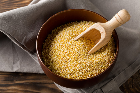 Pile of golden millet, a gluten free grain seed, in wooden bowl on grey kitchen towel on rustic brown wooden kitchen tableの写真素材