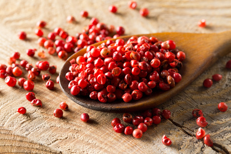Pink or rose brazilian red peppercorns (schinus terebinthifolius) in wooden spoon on rustic wooden table background - selective focusの写真素材
