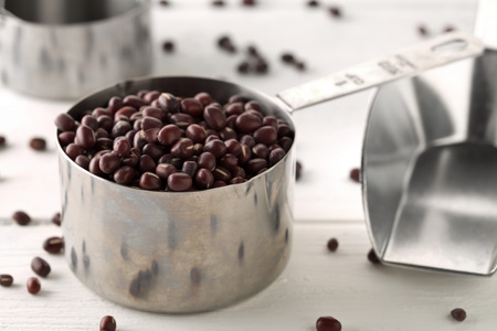Raw, uncooked, dried adzuki (red mung) beans in metal measurement cups on white wooden table background with selective focusの写真素材