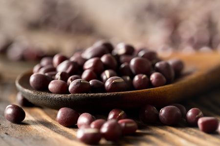 Raw, uncooked, dried adzuki (red mung) beans in wooden spoon on rustic wood table background...