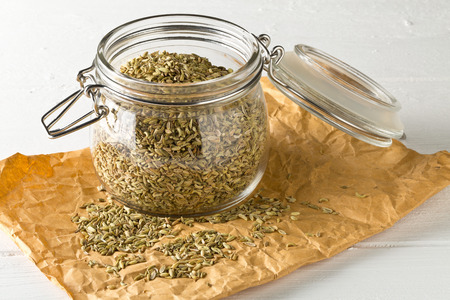 Dried fennel seeds in glass storage jar on white wooden table backgroundの写真素材