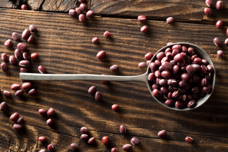 Raw, uncooked, dried adzuki (red mung) beans in metal spoon on rustic wood table background top view...
