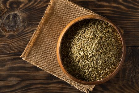 Dried fennel seeds in wooden bowl on rustic wooden table background top view flat lay from above with selective focusの写真素材
