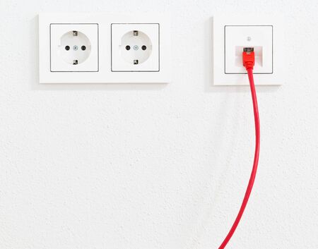 Red network cable in wall outlet for office or private home lan ethernet connection with power outlets flat view on white plaster wall backgroundの写真素材