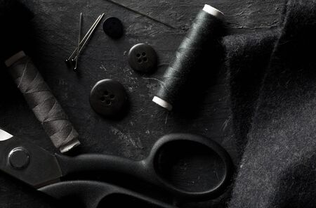 Flat lay top view sewing tools with buttons, textile fabric, thread, needles and scissors on black dark wooden tableの写真素材