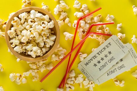 Movie tickets, soda drink plastic straws and popcorn on yellow table background. Home theatre movie or series night concept. Flat lay top view from above.の写真素材