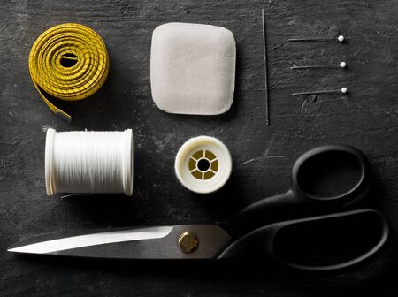 Flat lay top view sewing tools with measuring tape, chalk, thread, needles and scissors on black...