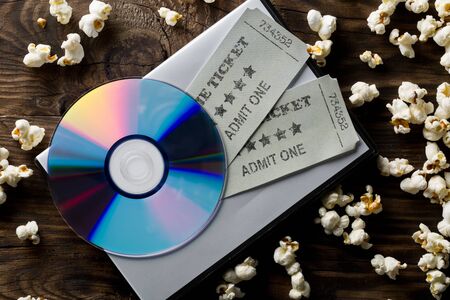 Movie tickets, DVD or blu ray disc and popcorn on dark wooden table background. Home theatre movie or series night concept. Flat lay top view from above.の写真素材