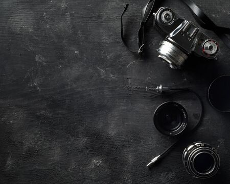Retro analog film camera with lenses and photography equipment on dark wooden table background with...