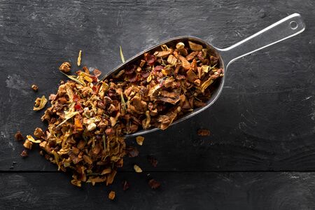 Heap of dried fruit tea infusion with oranges and strawberries mixed with tea leaves and assorted herbs in metal scoop on black wooden table background flat lay top view from aboveの写真素材