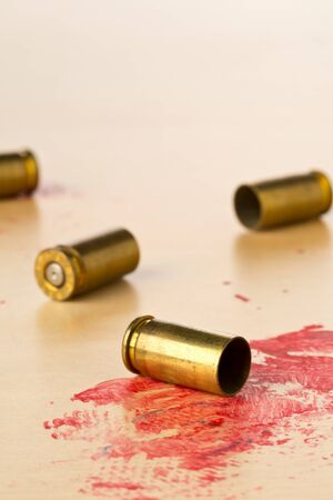 Empty, fired, blood covered 9mm bullet casings on wooden floor background at CSI crime scene...