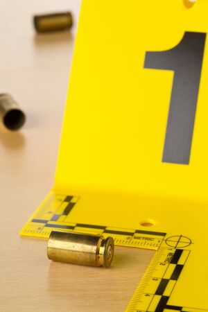 Crime scene investigation CSI evidence marker with empty, fired 9mm bullet casings on wooden floor...