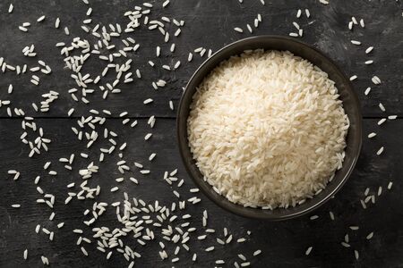 White uncooked, raw long grain rice in black bowl on rustic, black wooden table with copy space top view flat lay from above - selective focusの写真素材