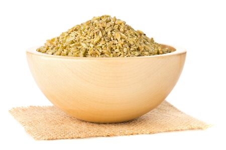 Heap of uncooked, raw freekeh or firik, roasted wheat grain, in wooden bowl over white backgroundの写真素材