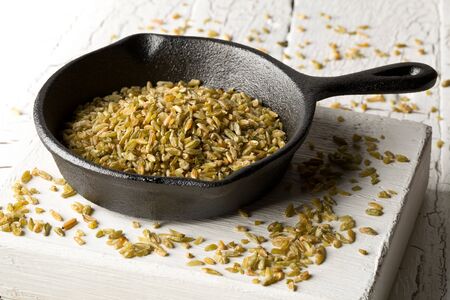 Uncooked, raw freekeh or firik, roasted wheat grain, in metal pan on white rustic table background with selective focusの写真素材