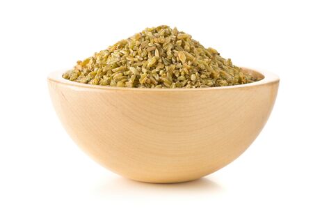 Heap of uncooked, raw freekeh or firik, roasted wheat grain, in wooden bowl over white backgroundの写真素材