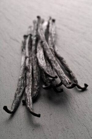 Bundle of dried bourbon vanilla beans or pods on black stone board with selective focus