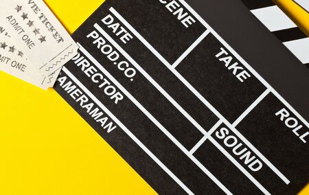 Single, black, opened movie clapper or clapper-board with movie cinema tickets flat lay top down view from above on yellow or orange backgroundの写真素材