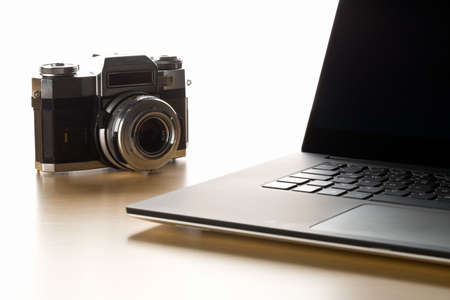 Retro analog SLR camera next to laptop on wooden desk in office, digital photography or image processing concept, selective focusの写真素材