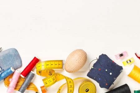 Collection of sewing tools with yarn, needles, scissors and tape measure over white wooden table...