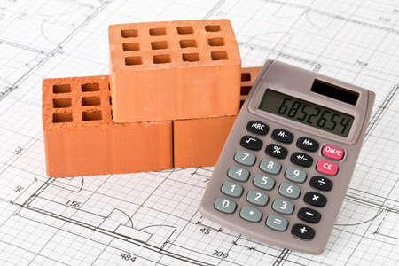 Calculator with bricks on architectural house building blueprint plan background, real estate or house building costs conceptの写真素材