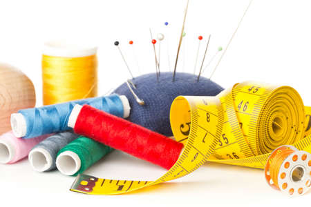 Close up of collection of sewing tools with yarn, needles, scissors and tape measure over white...