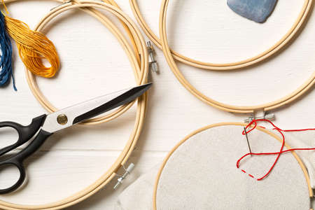Round stitching or embroidery frame with red stitching and sewing tools on white wooden table backgroundの写真素材