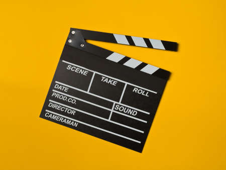 Single, black, opened movie clapper or clapper-board flat lay top down view from above on yellow or...