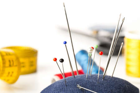 Close up of collection of sewign needles with sewing tools in the background over white background with selective focusの写真素材