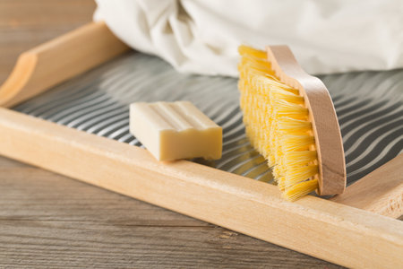 Close up of wood and metal washboard or wash board with brush, piece of washing soap and white shirt on wooden background, selective focusの写真素材