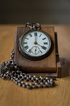 Antique pocket watch with roman numerals, and a metal chain on a wooden stand