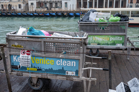 Venice, Italy- Feb 23, 2023: Waste bins filled with trash next to the Grand Canal in Venice ready to...