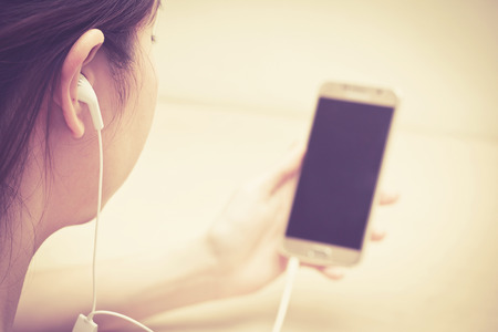 girl listening by earphone and look at smartphone in handの写真素材
