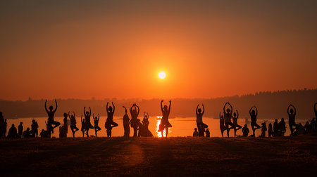 Silhouette of a group of people practicing yoga at sunset.の素材