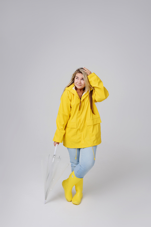 Blonde woman wearing yellow raincoat holding transparent umbrella checking weather if it is raining. Protected against rain and hurricaneの写真素材