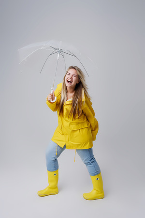 Blonde woman wearing yellow raincoat holding transparent umbrella checking weather if it is raining. Protected against rain and hurricaneの写真素材