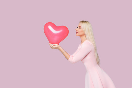 Beautiful young blond woman with pink heart shape air balloon on pink background. Woman on Valentine Day. Symbol of love. Space for textの写真素材