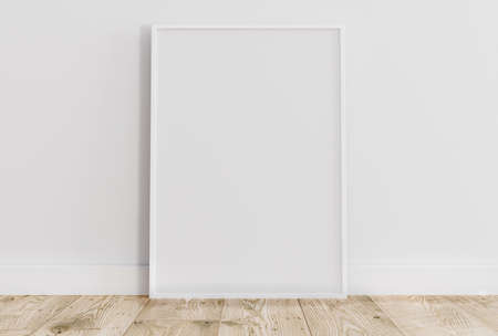Empty thin white frame on light wooden floor with white wall behind it. Empty poster frame mockup. Empty picture frame mockup. Blank photo frame.の写真素材