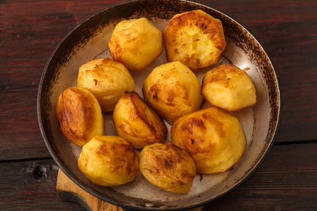 Savory golden roasted potato slices seasoned with fresh rosemary and bacon pieces and served in an old frying pan on a rustic wood table with copy space and a striped cloth.の写真素材
