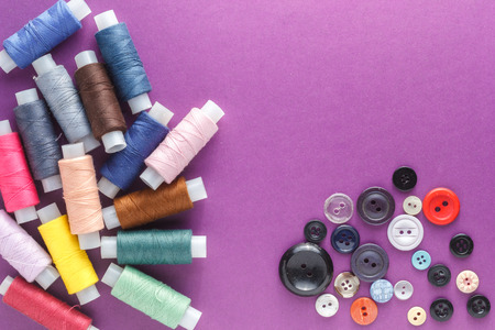 Many different colorful sewing threads and a variety of buttons on a purple background.の写真素材