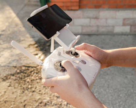 Man holding in his hands remote controller joystick transmitter flying the drone with sun shining bright day outdoors.の写真素材